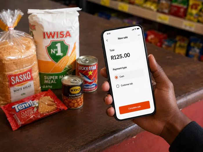 Spaza Tap sale recording screen on a phone beside everyday shop items.